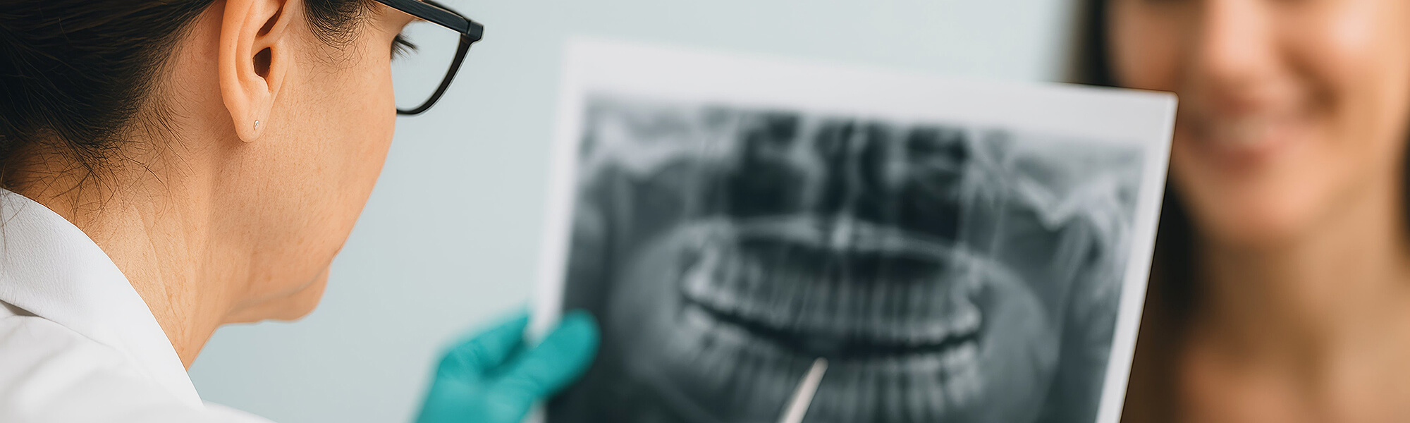 Zahnärztin mit Brille zeigt einer Patientin ein Röntgenbild und erklärt den Befund, Patientin lächelt