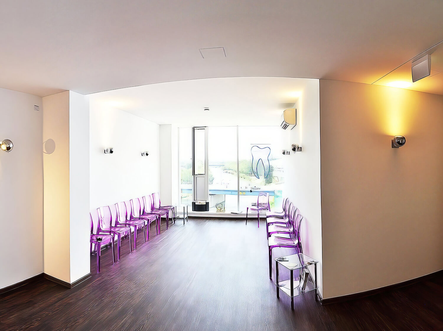 Wartebereich der Zahnarztpraxis mit großen Fenstern, lilafarbenen transparenten Stühlen und hellem Ambiente