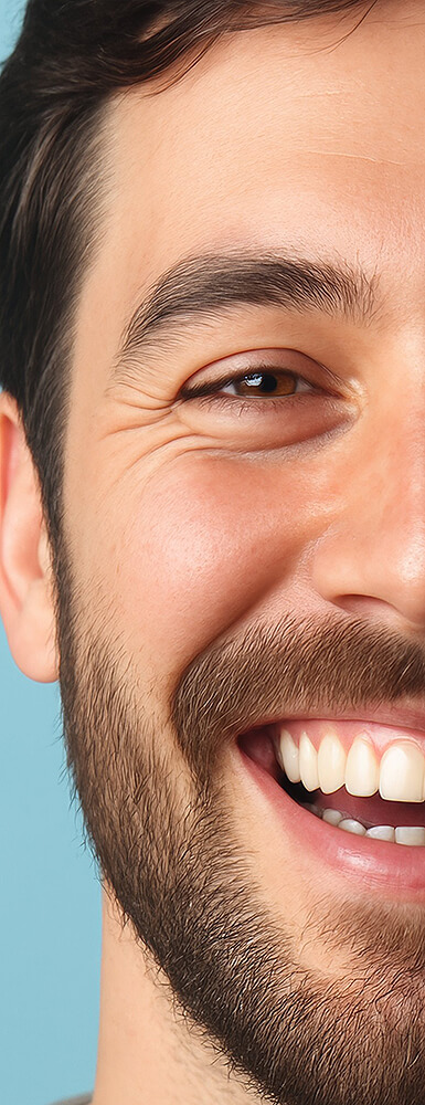 Junger Mann mit Bart, freundlich lächelnd, Nahaufnahme seiner rechten Gesichtshälfte auf blauem Hintergrund.