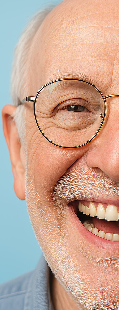 Älterer Mann mit Brille und grauem Bart lacht herzlich, Nahaufnahme der rechten Gesichtshälfte vor blauem Hintergrund.