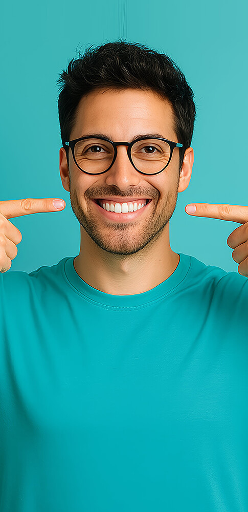 Lächelnder Mann mit Brille zeigt mit beiden Fingern auf sein strahlendes Lächeln vor blaugrünem Hintergrund.