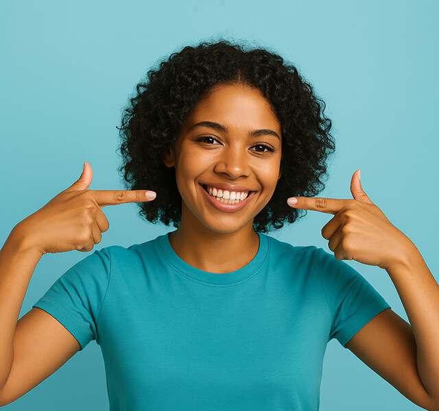Lächelnde Person mit Locken zeigt mit beiden Händen auf ihre Zähne, türkisfarbener Hintergrund.